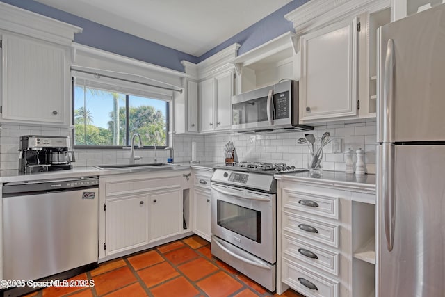 kitchen featuring stainless steel appliances, tasteful backsplash, dark tile patterned flooring, white cabinets, and sink