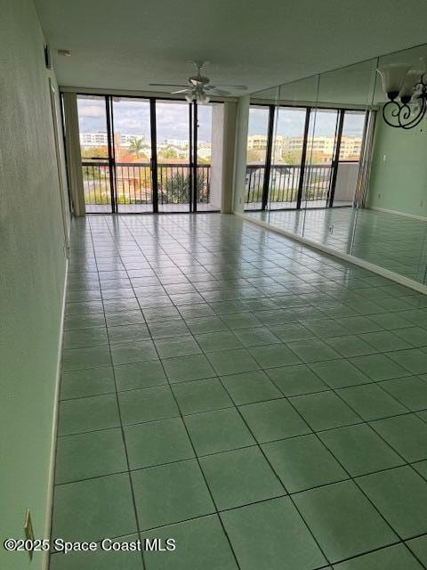 tiled spare room with ceiling fan and a wall of windows