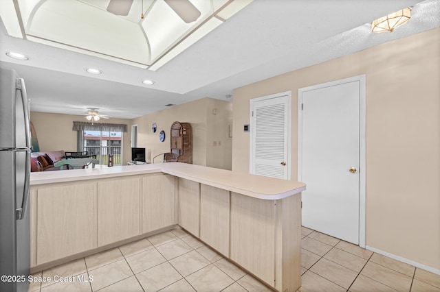 kitchen featuring light brown cabinetry, stainless steel fridge, kitchen peninsula, ceiling fan, and light tile patterned floors