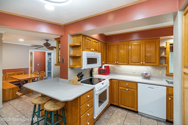 kitchen with kitchen peninsula, ceiling fan, white appliances, light tile patterned flooring, and a breakfast bar