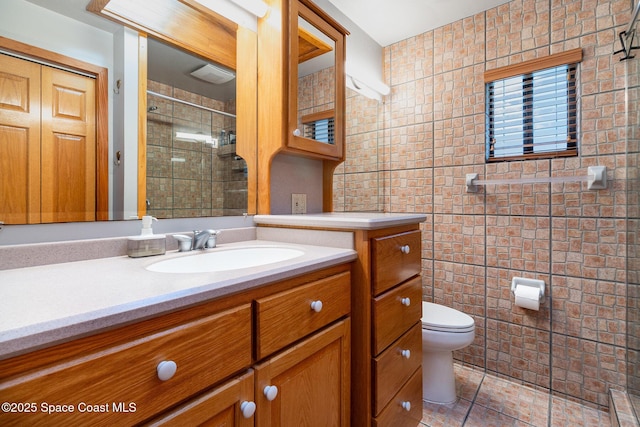 bathroom with toilet, a shower with door, tile patterned flooring, tile walls, and vanity