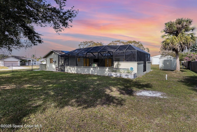 back house at dusk with a lawn, a storage unit, and glass enclosure