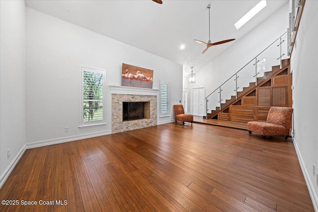 unfurnished living room featuring a skylight, ceiling fan, a fireplace, and high vaulted ceiling