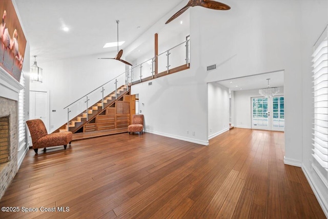 unfurnished living room featuring a high ceiling, french doors, ceiling fan with notable chandelier, a fireplace, and wood-type flooring