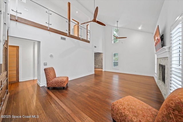 living room featuring wood-type flooring, high vaulted ceiling, a brick fireplace, and ceiling fan