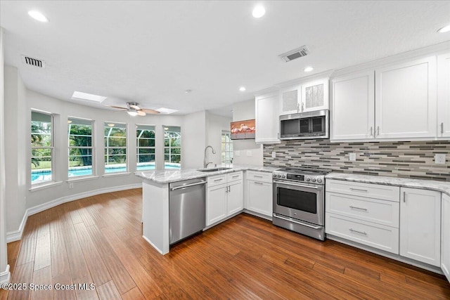 kitchen with white cabinets, kitchen peninsula, stainless steel appliances, and a skylight