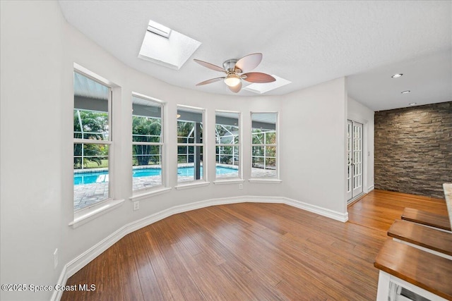 empty room with a skylight, ceiling fan, hardwood / wood-style floors, and a textured ceiling