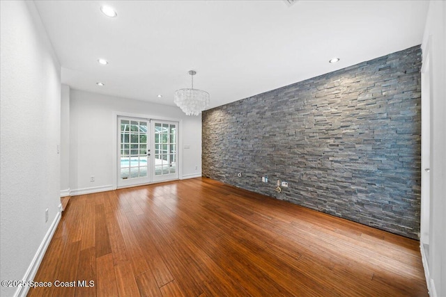 spare room featuring french doors, hardwood / wood-style flooring, and a notable chandelier