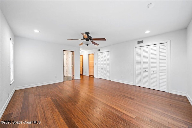 unfurnished bedroom with hardwood / wood-style floors, two closets, and ceiling fan