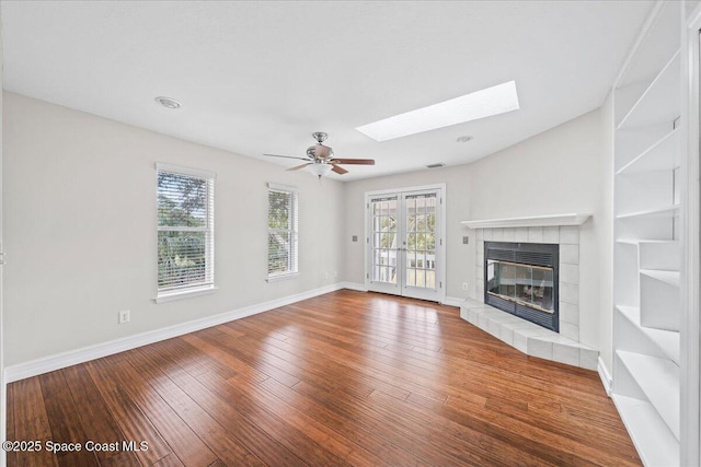 unfurnished living room with a skylight, ceiling fan, french doors, wood-type flooring, and a fireplace