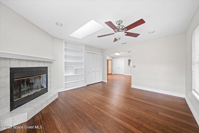 unfurnished living room with a skylight, ceiling fan, hardwood / wood-style flooring, and a tiled fireplace