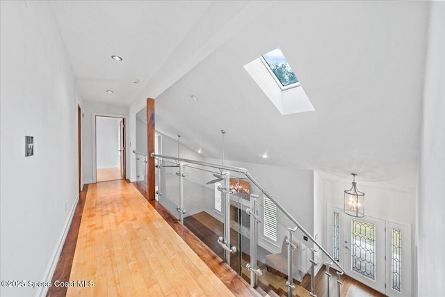 hallway featuring wood-type flooring, an inviting chandelier, a skylight, and high vaulted ceiling