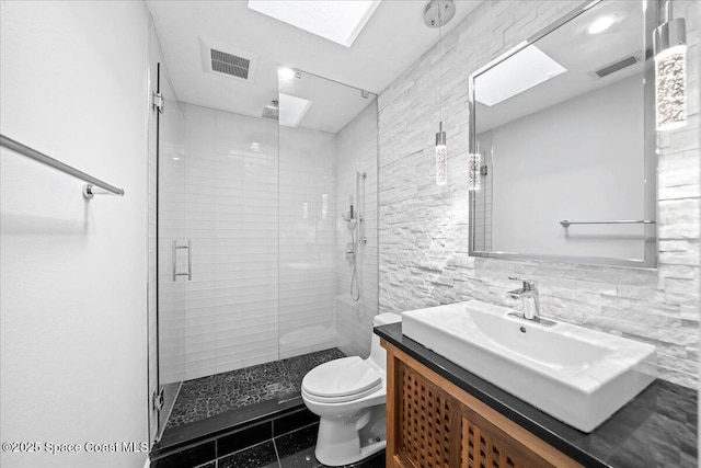 bathroom with a skylight, tile patterned floors, toilet, vanity, and a shower with shower door