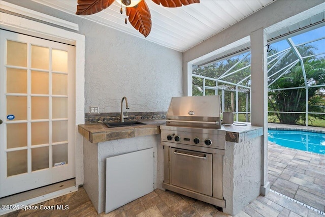 view of patio / terrace with area for grilling, a lanai, ceiling fan, sink, and grilling area