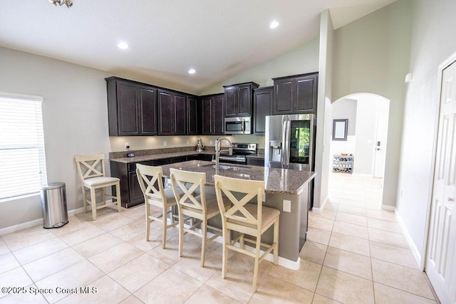 kitchen with a kitchen breakfast bar, stainless steel appliances, an island with sink, sink, and light tile patterned flooring