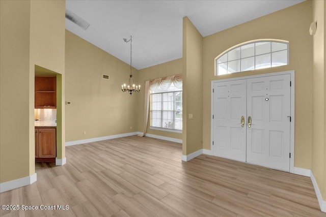 entrance foyer with light wood-type flooring, high vaulted ceiling, and a notable chandelier