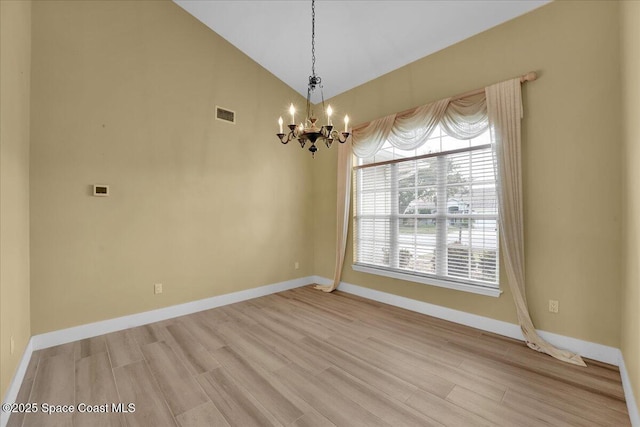 empty room featuring lofted ceiling, light wood-type flooring, and a notable chandelier