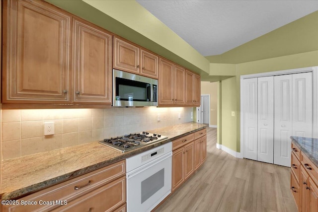 kitchen featuring lofted ceiling, tasteful backsplash, light hardwood / wood-style floors, appliances with stainless steel finishes, and stone countertops