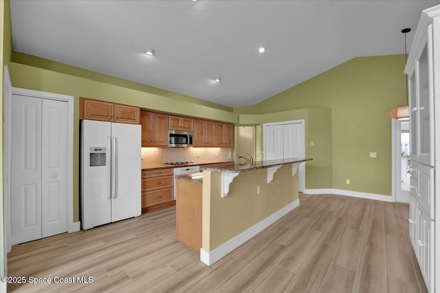 kitchen featuring appliances with stainless steel finishes, lofted ceiling, tasteful backsplash, a kitchen breakfast bar, and a kitchen island with sink