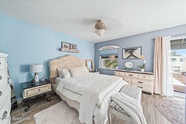 bedroom featuring ceiling fan, access to outside, light hardwood / wood-style floors, and a textured ceiling