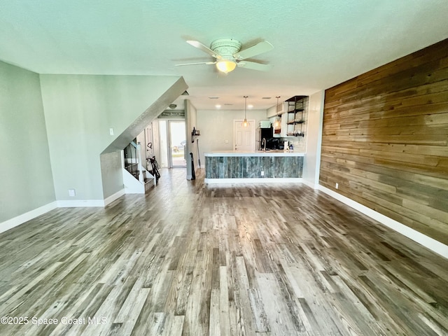 unfurnished living room featuring ceiling fan, wood-type flooring, and wooden walls