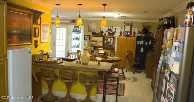 kitchen featuring pendant lighting, refrigerator, ornamental molding, a kitchen bar, and stainless steel refrigerator