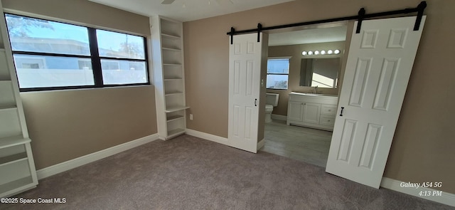 unfurnished bedroom featuring connected bathroom, light carpet, sink, ceiling fan, and a barn door