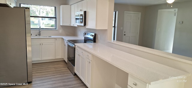 kitchen with light wood-type flooring, stainless steel appliances, white cabinetry, and sink