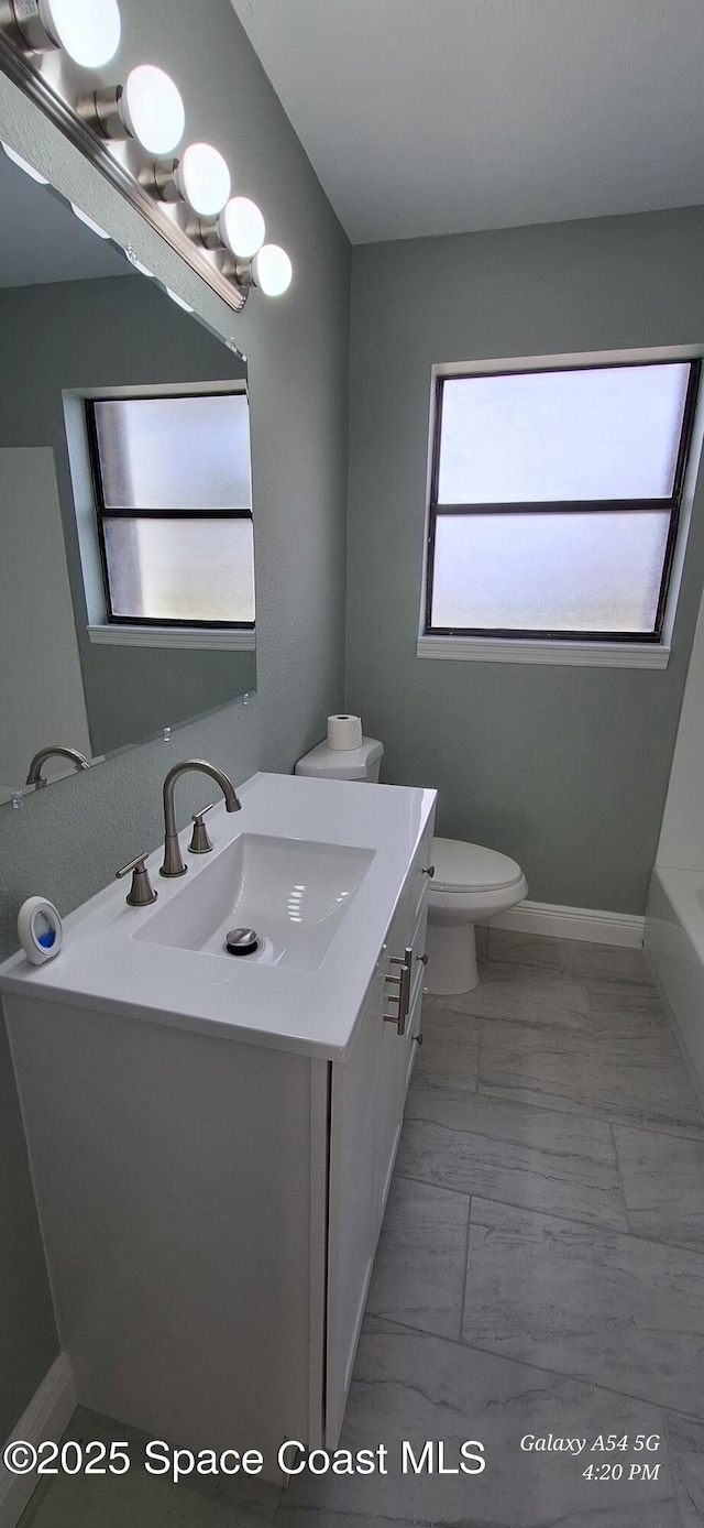 bathroom featuring a wealth of natural light, toilet, vanity, and a tub to relax in