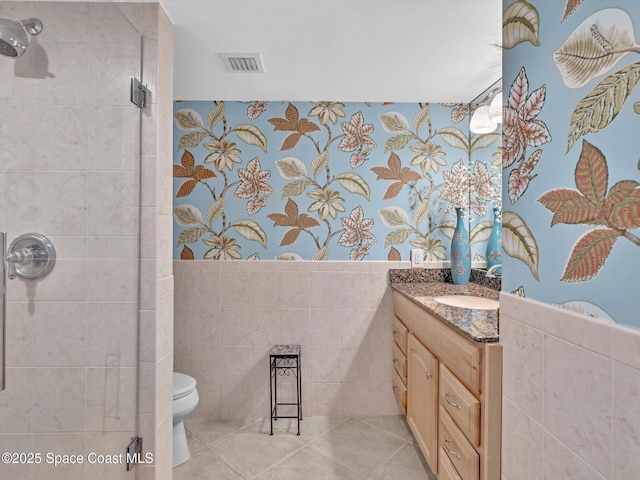 bathroom with tile patterned floors, toilet, a shower with door, vanity, and tile walls