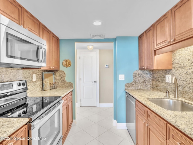 kitchen with light stone countertops, sink, stainless steel appliances, tasteful backsplash, and light tile patterned flooring