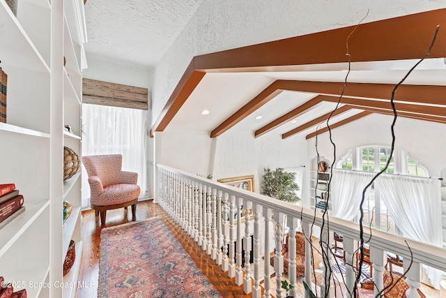 hall featuring wood-type flooring, lofted ceiling with beams, and a textured ceiling