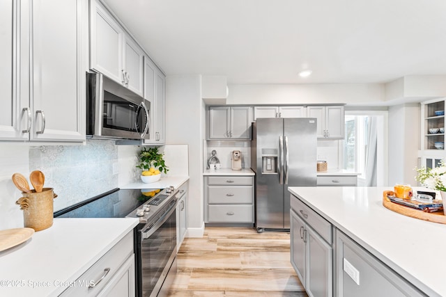 kitchen featuring gray cabinets, light hardwood / wood-style flooring, stainless steel appliances, and tasteful backsplash