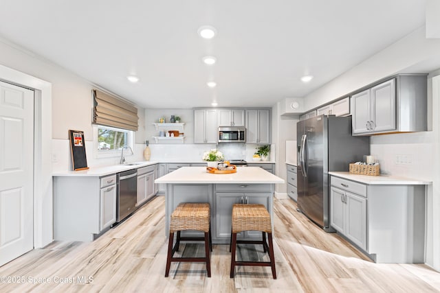 kitchen featuring stainless steel appliances, gray cabinetry, a center island, a kitchen breakfast bar, and sink