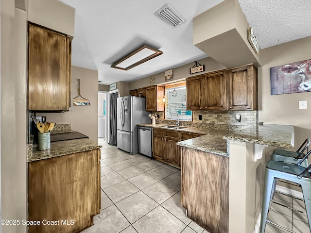 kitchen featuring kitchen peninsula, sink, a kitchen breakfast bar, stainless steel appliances, and light tile patterned floors