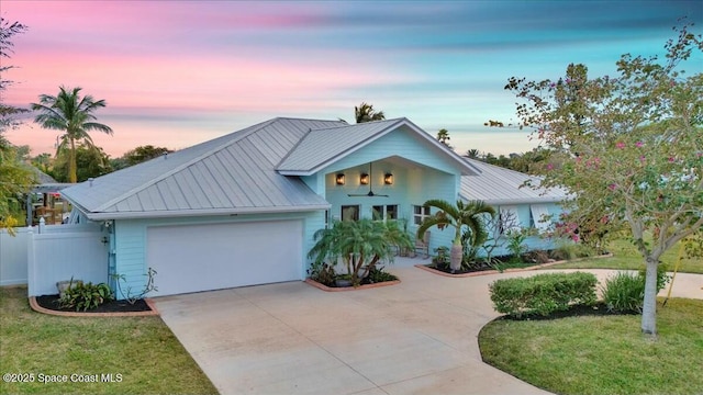 view of front of house with a garage, driveway, a lawn, metal roof, and fence