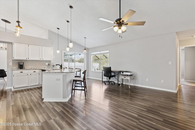 kitchen with hanging light fixtures, a breakfast bar area, light stone countertops, and white cabinets