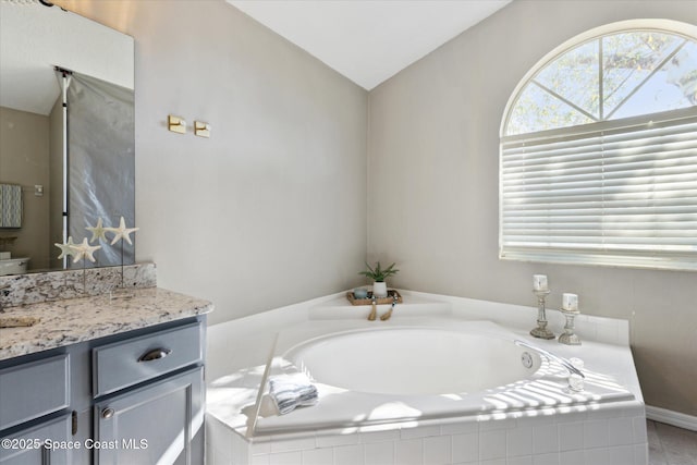 bathroom featuring tiled tub, vaulted ceiling, and vanity