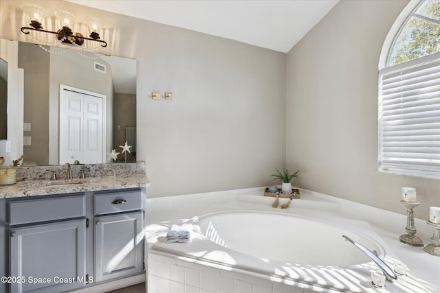 bathroom featuring lofted ceiling, vanity, and tiled tub