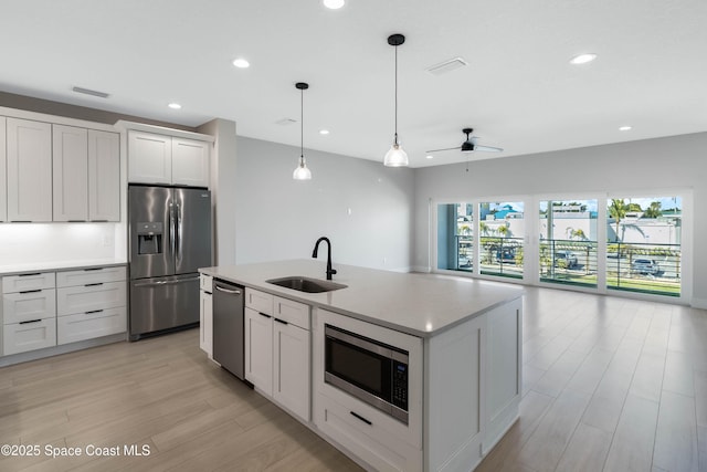 kitchen featuring appliances with stainless steel finishes, sink, decorative light fixtures, white cabinets, and a center island with sink