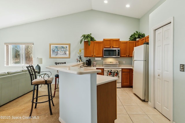 kitchen with white appliances, kitchen peninsula, vaulted ceiling, light tile patterned floors, and a kitchen breakfast bar