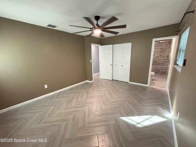 unfurnished bedroom featuring light parquet floors, ceiling fan, connected bathroom, a textured ceiling, and a closet