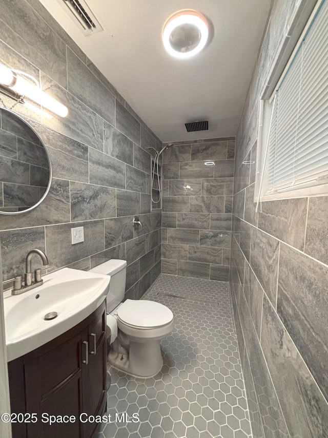 bathroom featuring toilet, tile walls, a tile shower, vanity, and tile patterned flooring