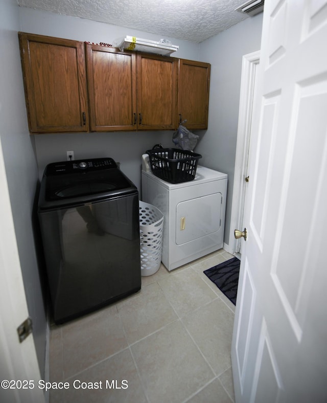 laundry room featuring a textured ceiling, cabinets, light tile patterned flooring, and washer and clothes dryer