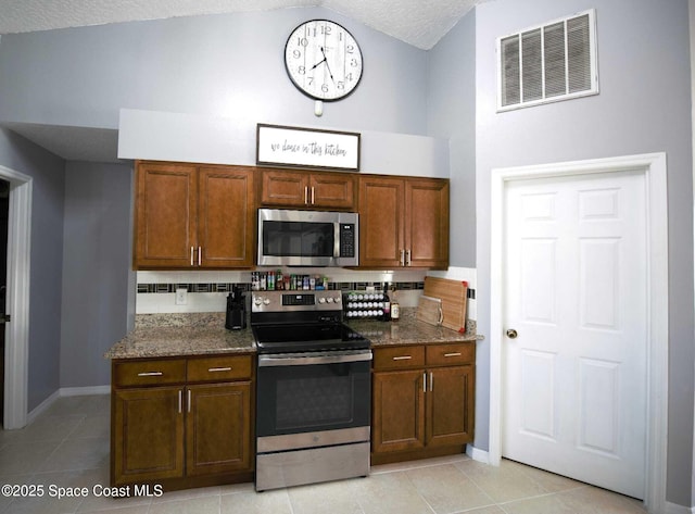 kitchen with light tile patterned floors, stainless steel appliances, a towering ceiling, and dark stone counters