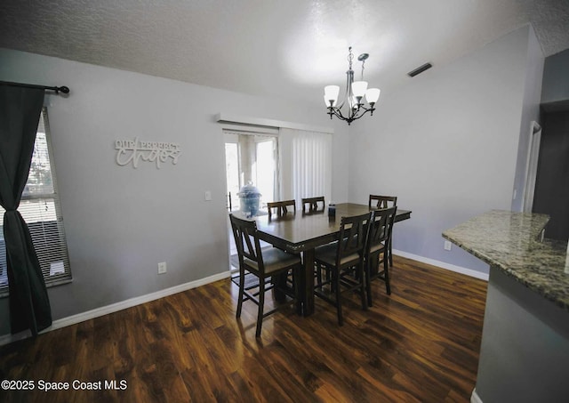 dining room featuring dark wood-type flooring, a textured ceiling, and a notable chandelier