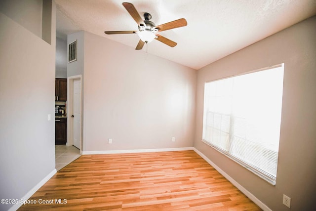 empty room with ceiling fan, vaulted ceiling, a textured ceiling, and light hardwood / wood-style flooring