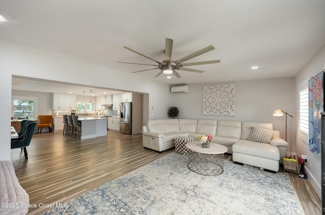 living room featuring ceiling fan, a wall unit AC, and hardwood / wood-style flooring