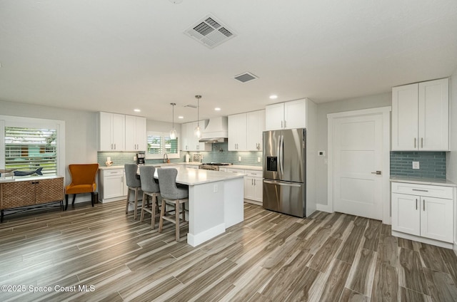 kitchen featuring stainless steel refrigerator with ice dispenser, custom exhaust hood, a center island, and white cabinets