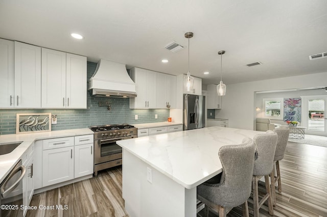 kitchen featuring a kitchen island, white cabinets, appliances with stainless steel finishes, and custom range hood